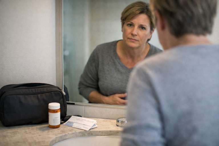 Toilet anxiety on journeys, person checking themselves in a bathroom mirror with travel washbag, medication and train ticket on the sink